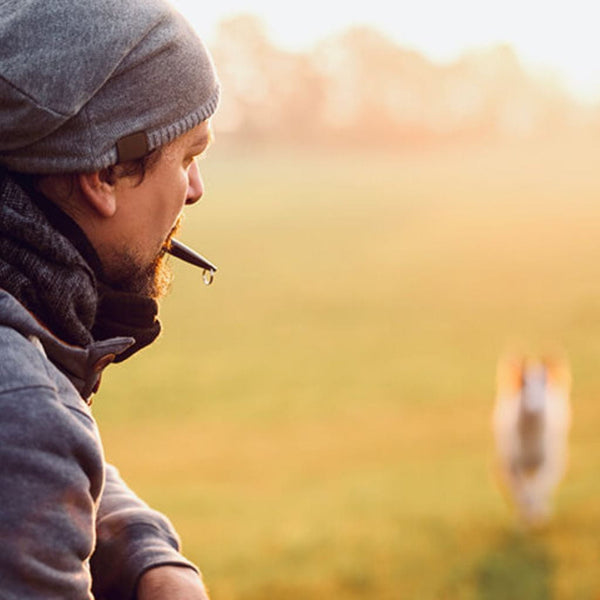 Man with whistle in his mouth training his dog to come when called.