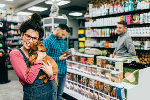 Female dog owner holding small brown dog in front pof pet shop counter.